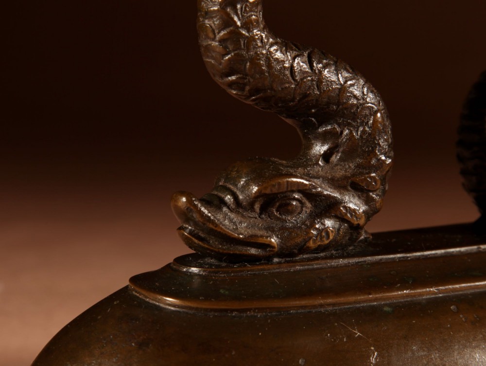 A nineteenth-century French bronze flat iron featuring twin dolphin-shaped supports, a cane-wrapped handle, and a rear door mechanism. View XII