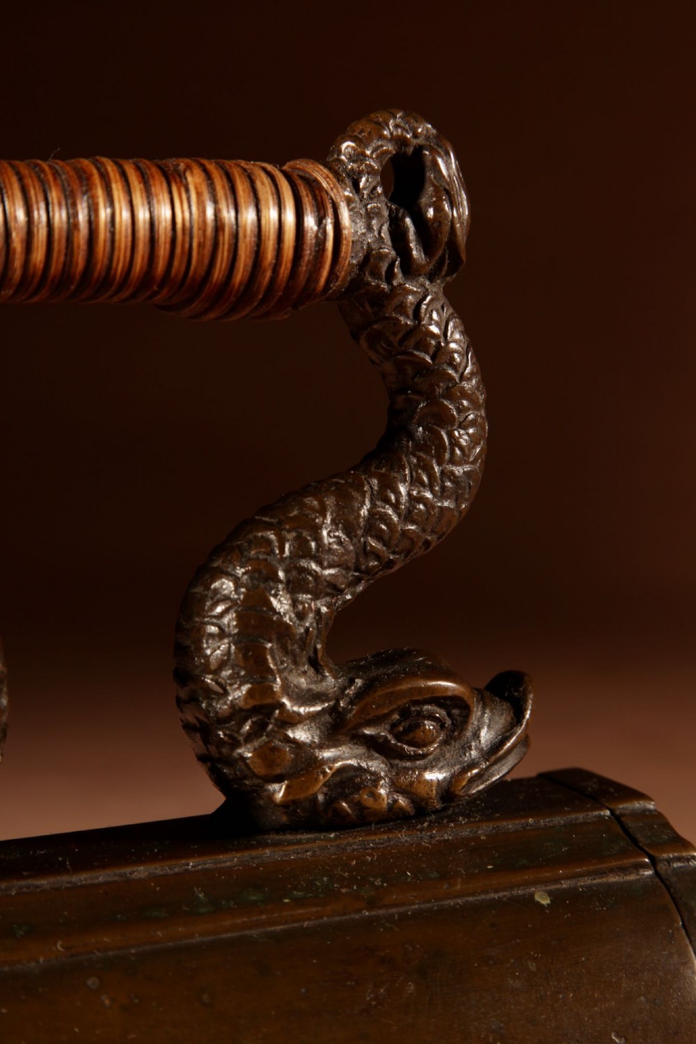A nineteenth-century French bronze flat iron featuring twin dolphin-shaped supports, a cane-wrapped handle, and a rear door mechanism. View XIII