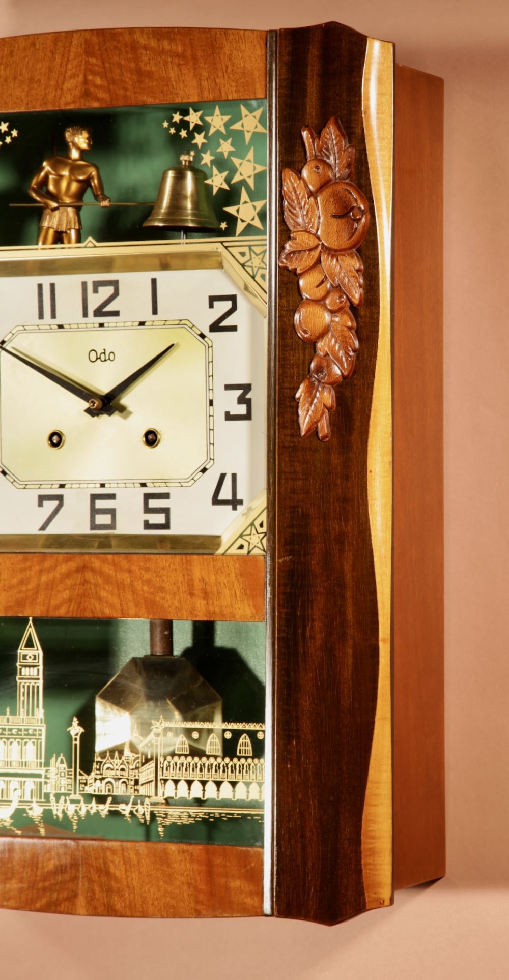 An Art Deco carved walnut wall clock by Odo featuring a brass automaton bell striker and a Venetian glass lower window. View V