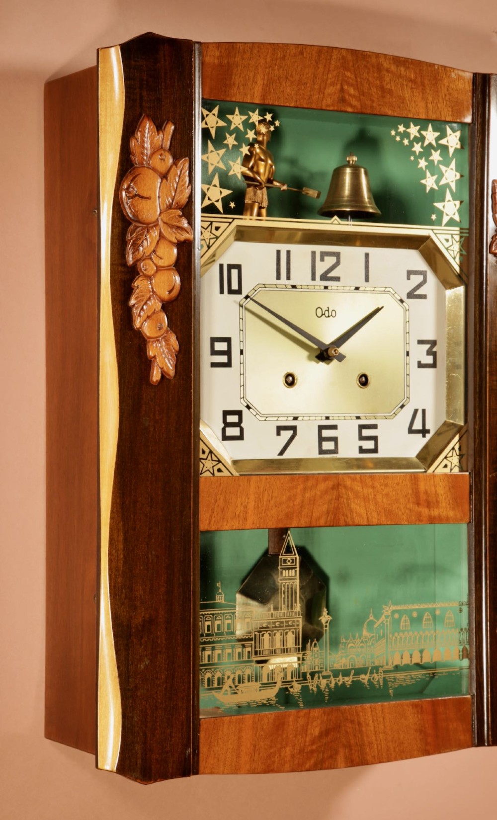 An Art Deco carved walnut wall clock by Odo featuring a brass automaton bell striker and a Venetian glass lower window. View VI