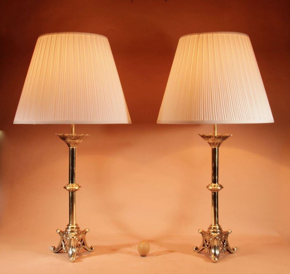 A pair of tall cast brass table lamps featuring Gothic architectural bases and pleated cream shades.
