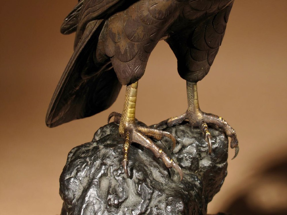 A patinated bronze sculpture depicting a hawk with detailed feather chasing perched atop a textured rocky outcrop, mounted on a carved wooden base. View IV