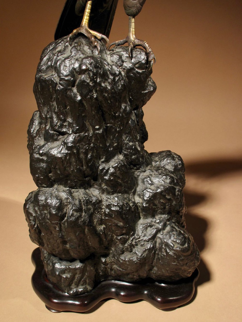 A patinated bronze sculpture depicting a hawk with detailed feather chasing perched atop a textured rocky outcrop, mounted on a carved wooden base. View VII