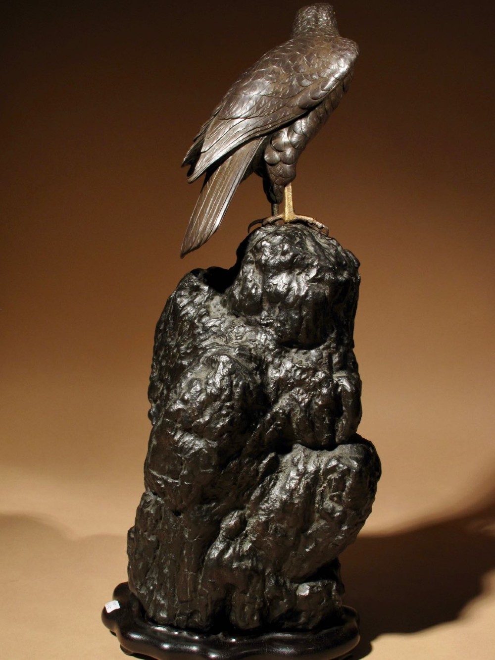 A patinated bronze sculpture depicting a hawk with detailed feather chasing perched atop a textured rocky outcrop, mounted on a carved wooden base. View VIII
