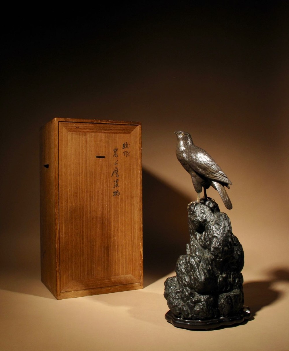 A patinated bronze sculpture depicting a hawk with detailed feather chasing perched atop a textured rocky outcrop, mounted on a carved wooden base. View X