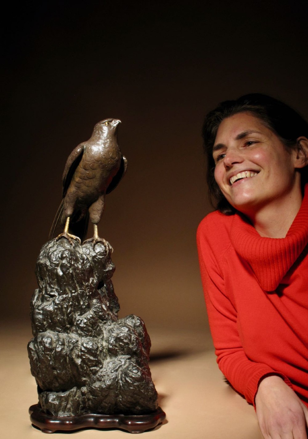 A patinated bronze sculpture depicting a hawk with detailed feather chasing perched atop a textured rocky outcrop, mounted on a carved wooden base. View XII