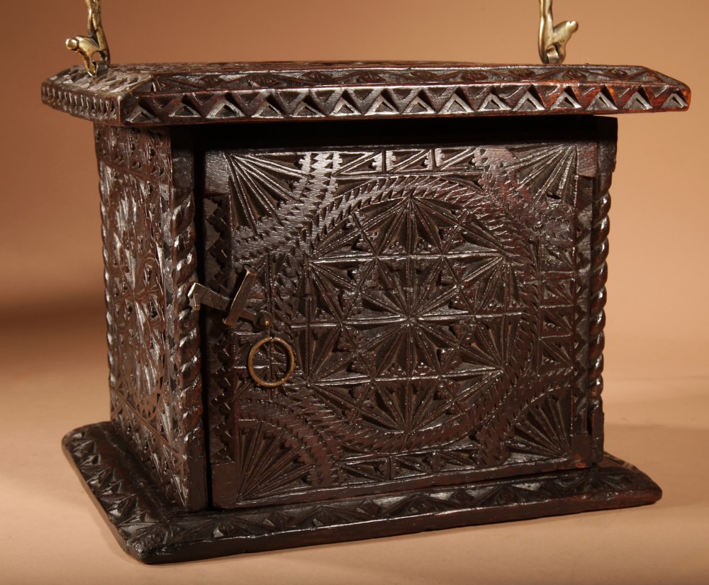 A square dark oak chip-carved foot stove with a hinged door, geometric rosette carvings, and a brass swing handle. View II