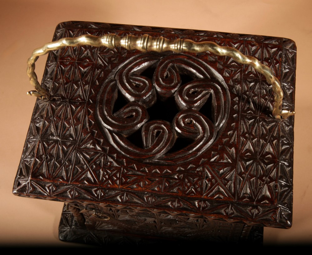 A square dark oak chip-carved foot stove with a hinged door, geometric rosette carvings, and a brass swing handle. View III