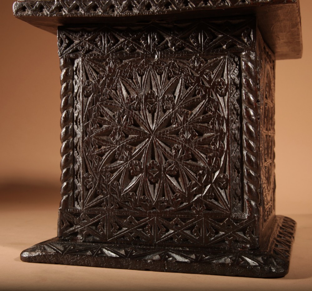 A square dark oak chip-carved foot stove with a hinged door, geometric rosette carvings, and a brass swing handle. View V