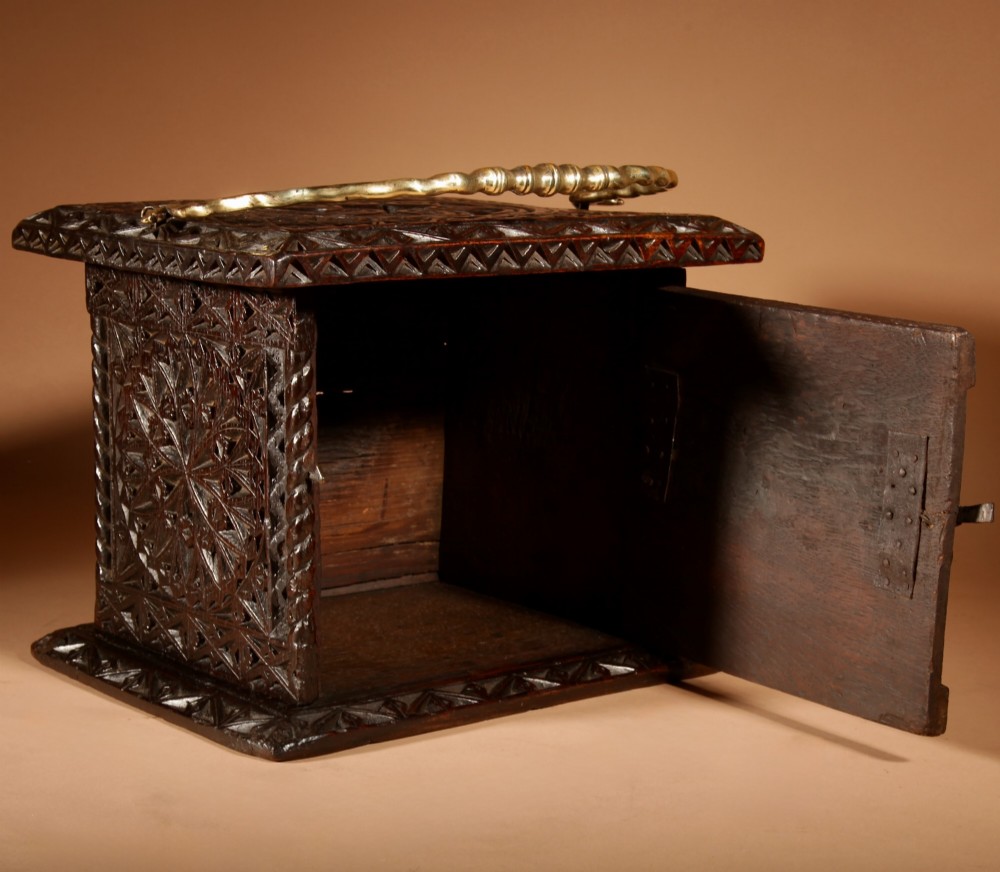 A square dark oak chip-carved foot stove with a hinged door, geometric rosette carvings, and a brass swing handle. View VII