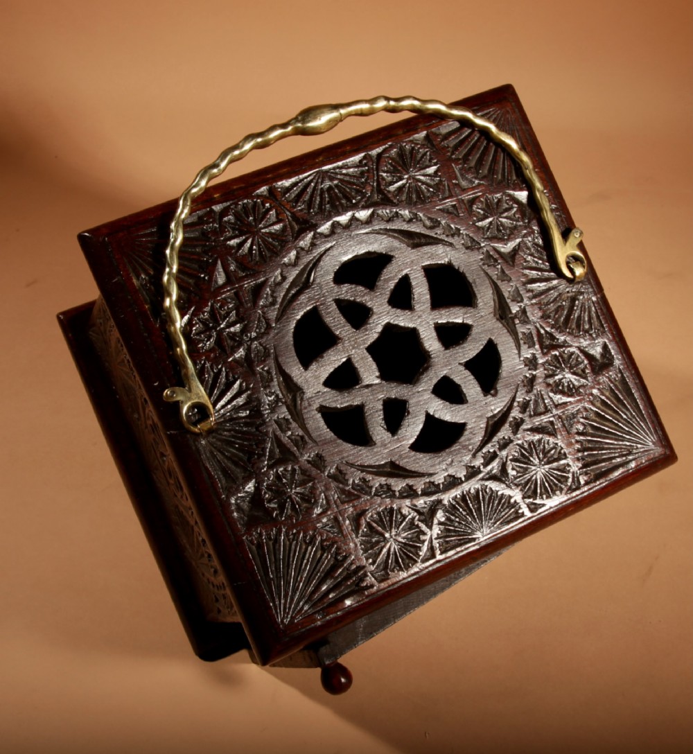 A dark carved oak foot stove featuring geometric chip carving, a pierced top lid, a hinged side door, and a twisted brass carrying handle. View II