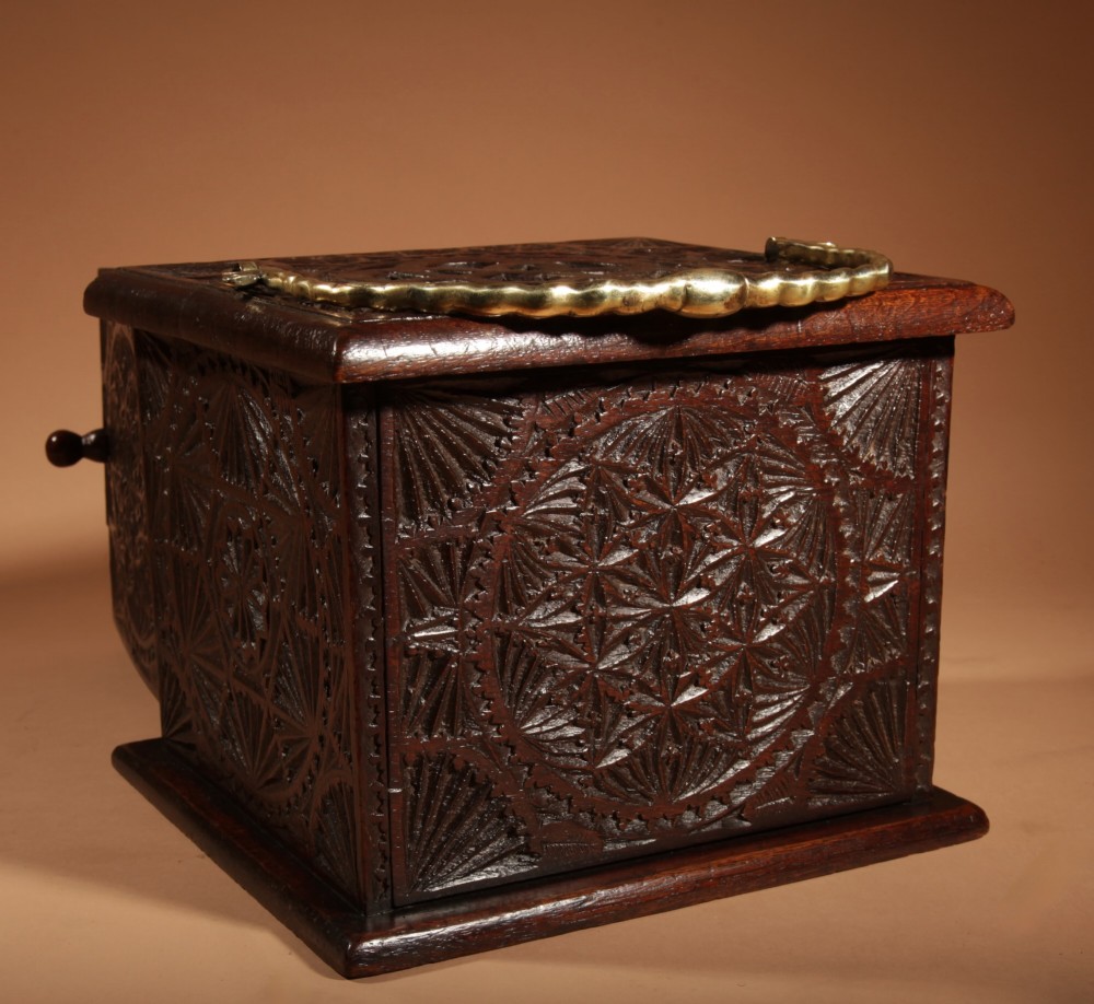 A dark carved oak foot stove featuring geometric chip carving, a pierced top lid, a hinged side door, and a twisted brass carrying handle. View III
