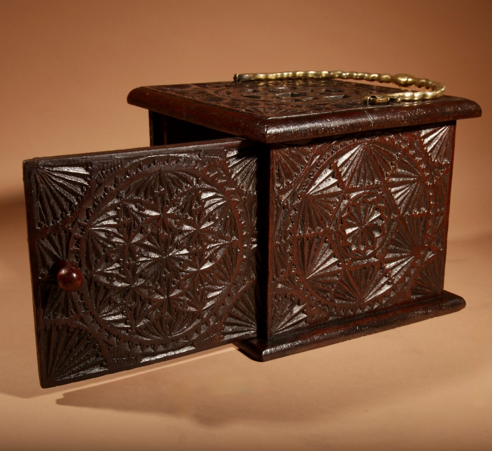 A dark carved oak foot stove featuring geometric chip carving, a pierced top lid, a hinged side door, and a twisted brass carrying handle. View IV