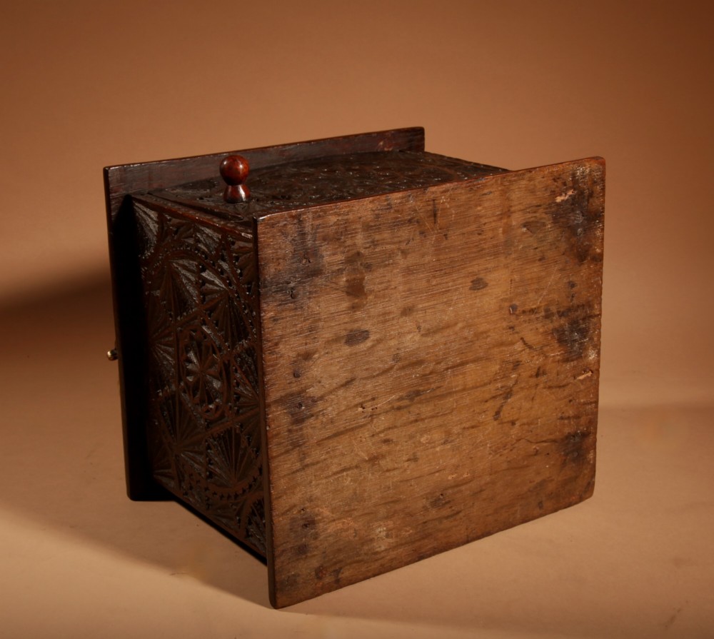 A dark carved oak foot stove featuring geometric chip carving, a pierced top lid, a hinged side door, and a twisted brass carrying handle. View VI