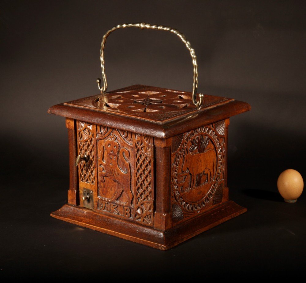 A square chip-carved wooden foot stove dated 1901 featuring relief carvings of animals and a brass carrying handle.