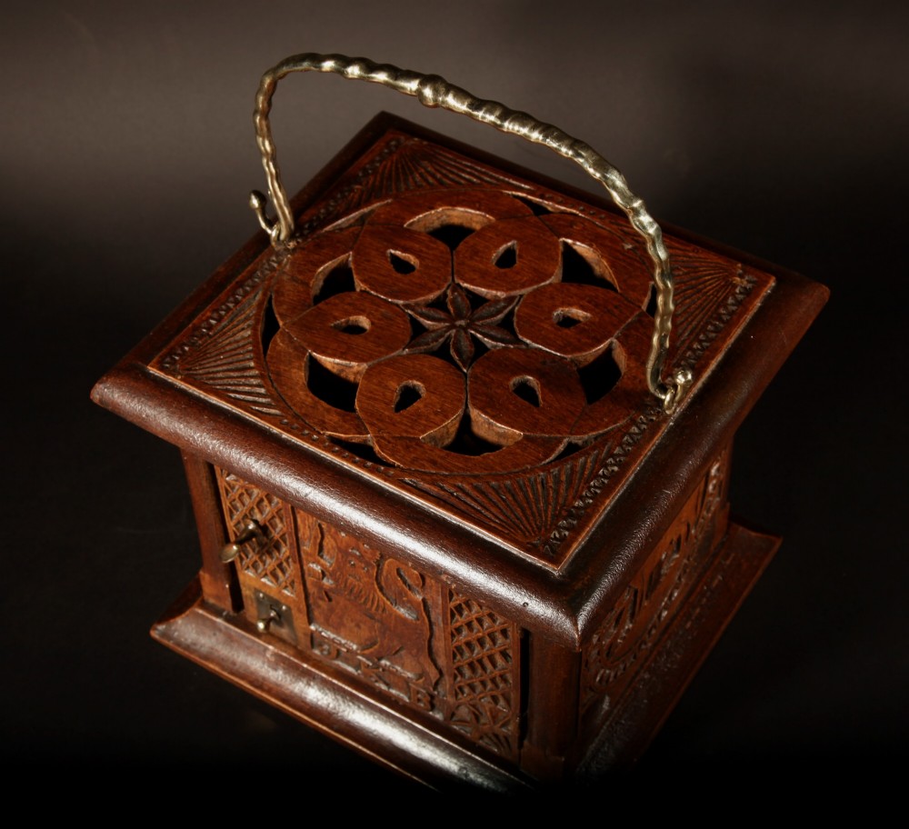 A square chip-carved wooden foot stove dated 1901 featuring relief carvings of animals and a brass carrying handle. View II