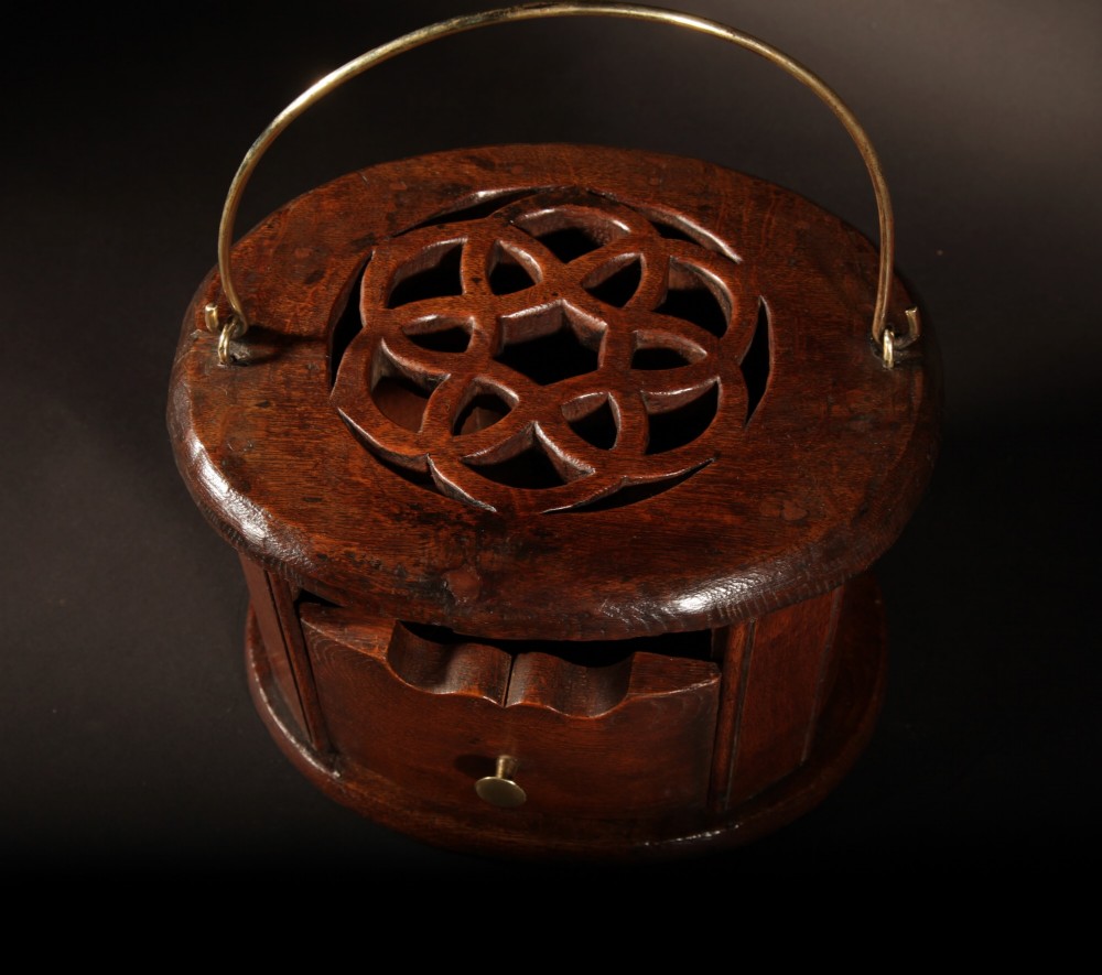 An oval dark oak foot stove featuring a carved geometric top aperture and an arched brass carrying handle. View II