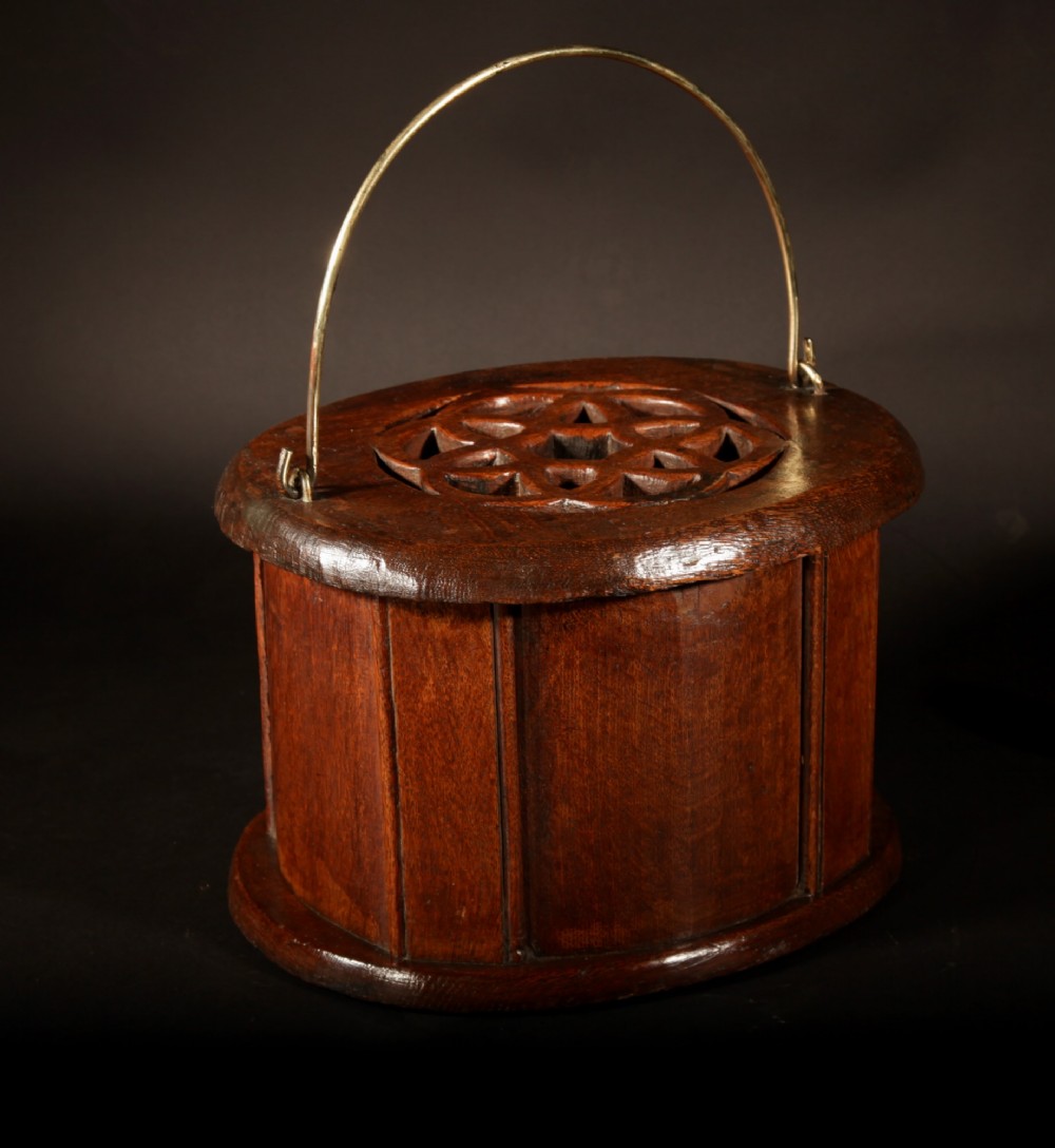 An oval dark oak foot stove featuring a carved geometric top aperture and an arched brass carrying handle. View III