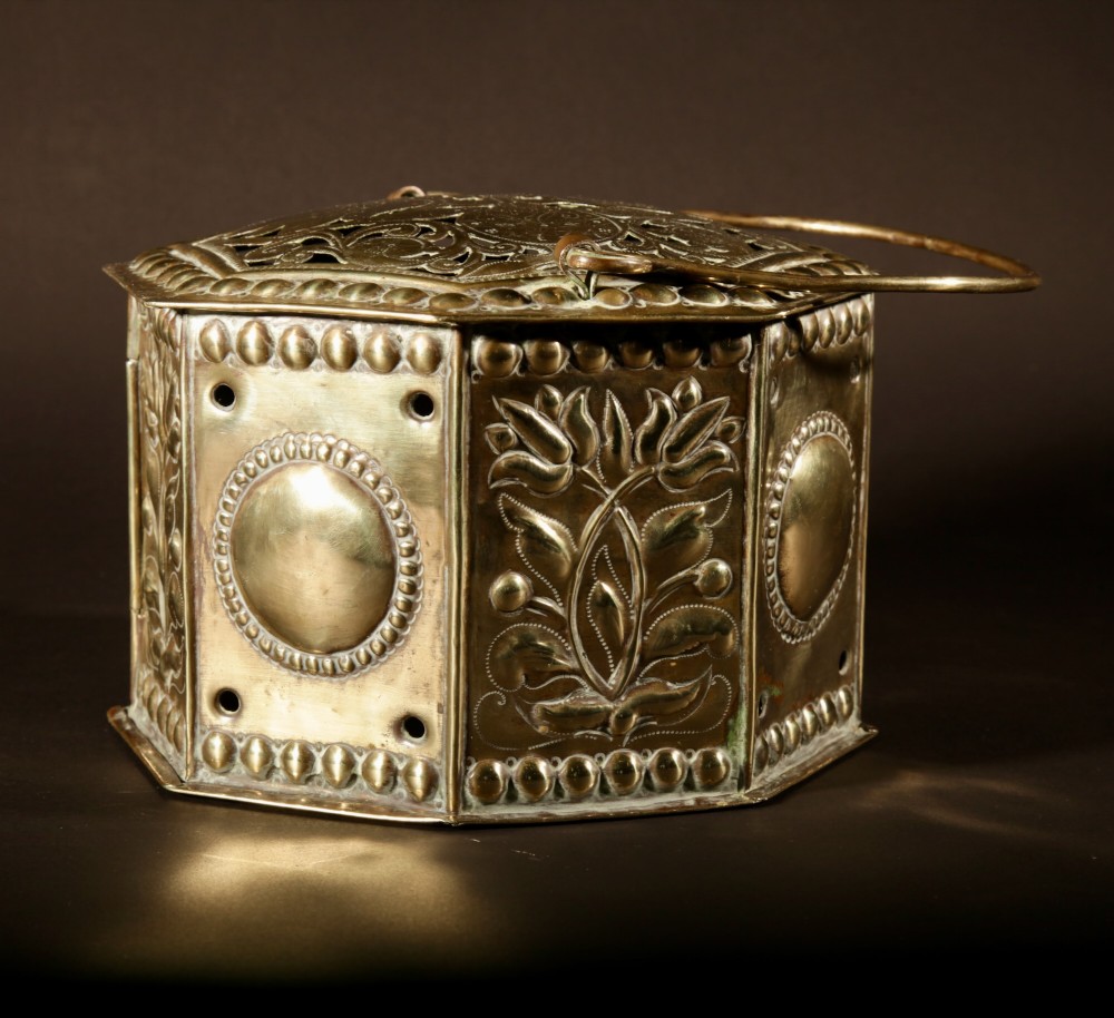 An 18th-century octagonal brass foot stove featuring hand-embossed floral panels, a pierced lid, and an overhead carrying handle. View IV