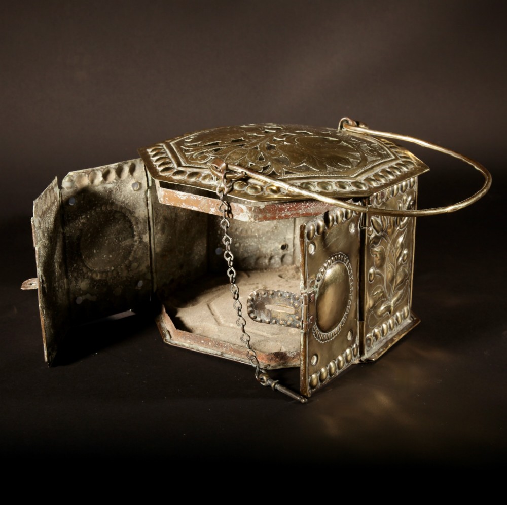 An 18th-century octagonal brass foot stove featuring hand-embossed floral panels, a pierced lid, and an overhead carrying handle. View VI