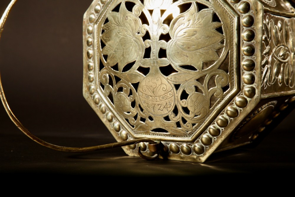 An 18th-century octagonal brass foot stove featuring hand-embossed floral panels, a pierced lid, and an overhead carrying handle. View VII