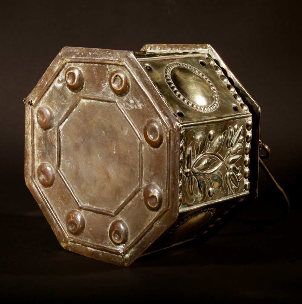 An 18th-century octagonal brass foot stove featuring hand-embossed floral panels, a pierced lid, and an overhead carrying handle. View VIII