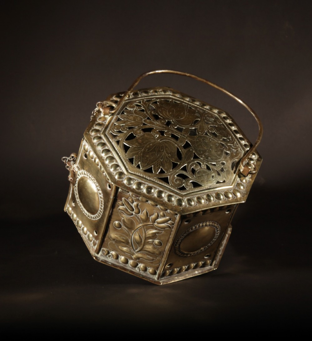 An 18th-century octagonal brass foot stove featuring hand-embossed floral panels, a pierced lid, and an overhead carrying handle. View IX