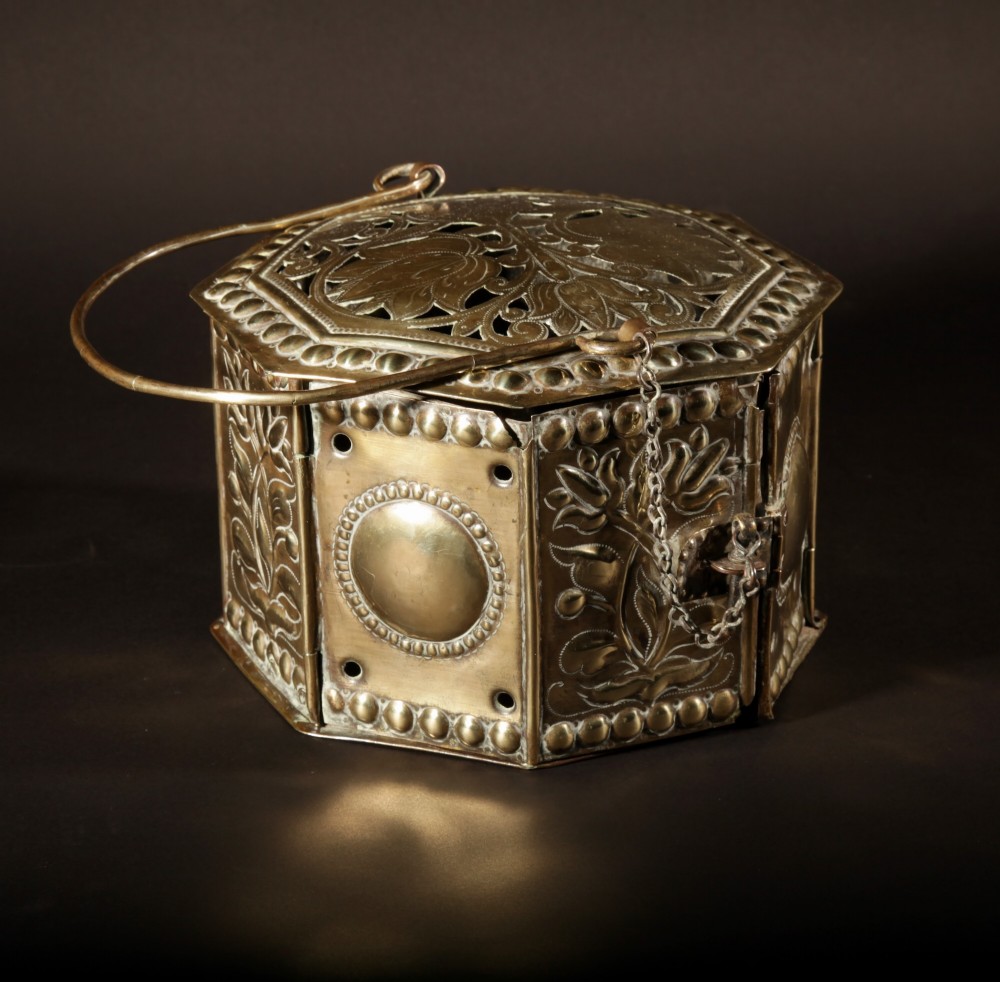 An 18th-century octagonal brass foot stove featuring hand-embossed floral panels, a pierced lid, and an overhead carrying handle. View X