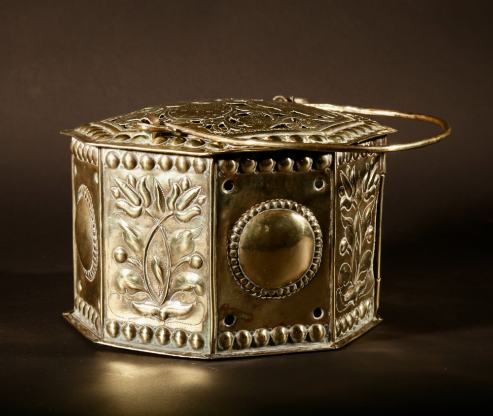 An 18th-century octagonal brass foot stove featuring hand-embossed floral panels, a pierced lid, and an overhead carrying handle. View XII