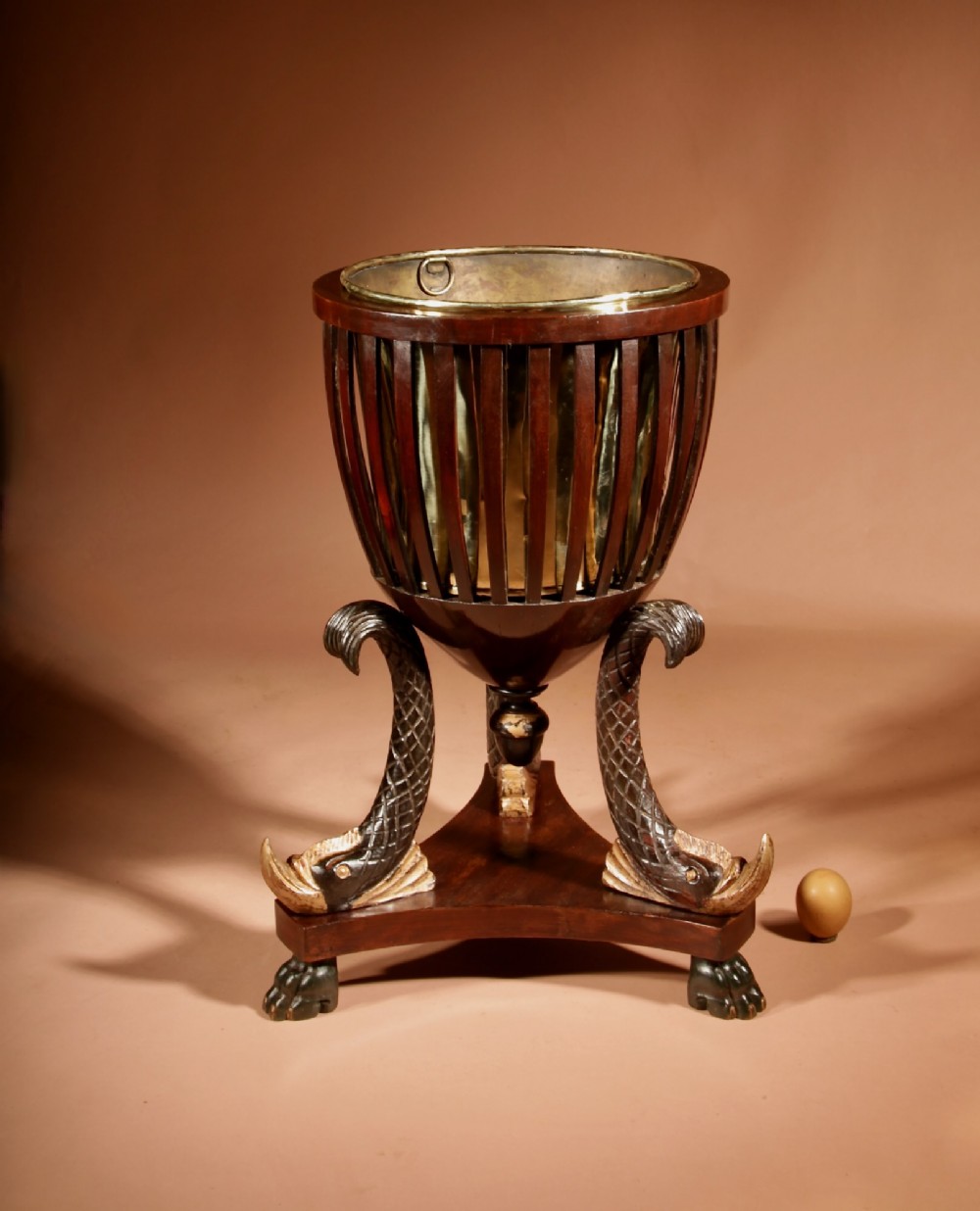 A French Empire mahogany slatted wine cooler featuring a brass liner and supported by three carved ebonised dolphin legs on a triform base with paw feet. View II