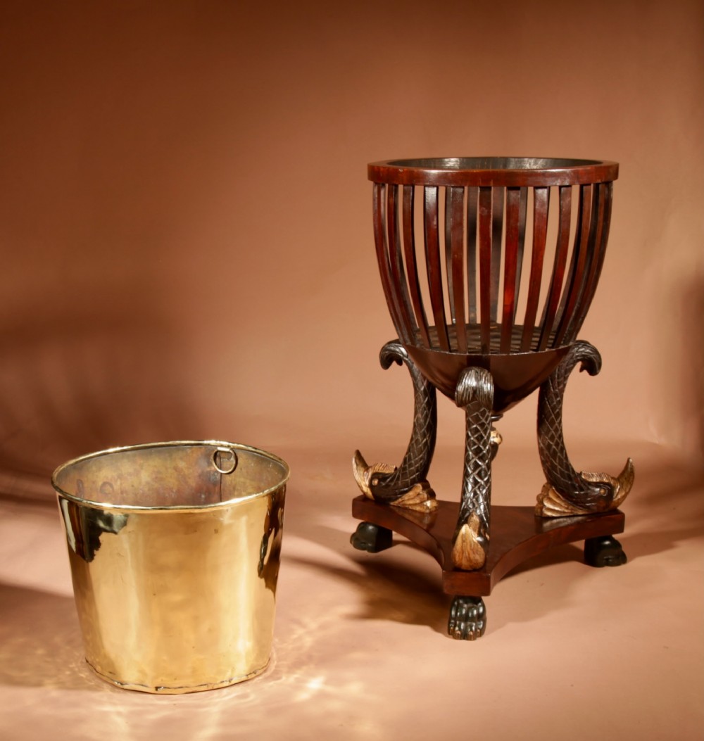 A French Empire mahogany slatted wine cooler featuring a brass liner and supported by three carved ebonised dolphin legs on a triform base with paw feet. View IX