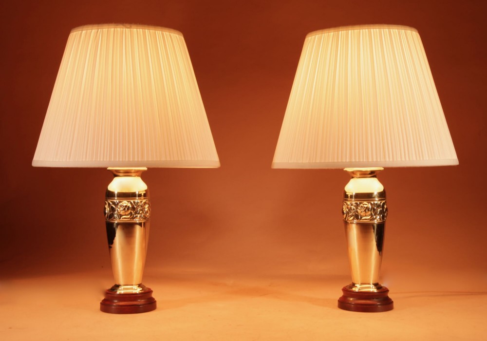 A pair of French Art Deco polished brass urn-form table lamps featuring embossed floral bands on wooden bases with pleated cream shades. View II