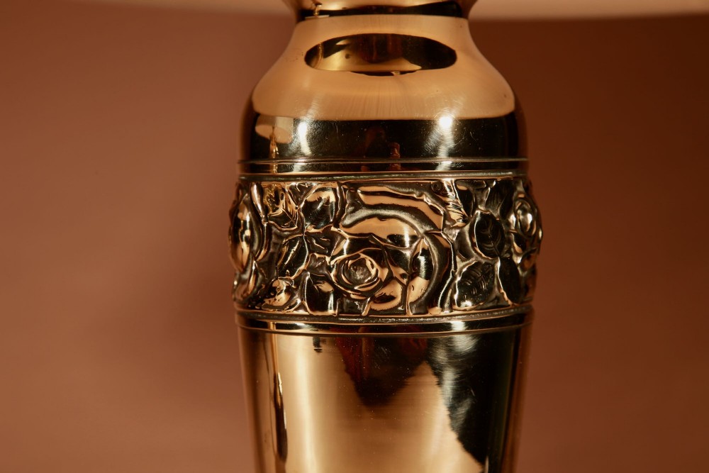 A pair of French Art Deco polished brass urn-form table lamps featuring embossed floral bands on wooden bases with pleated cream shades. View III