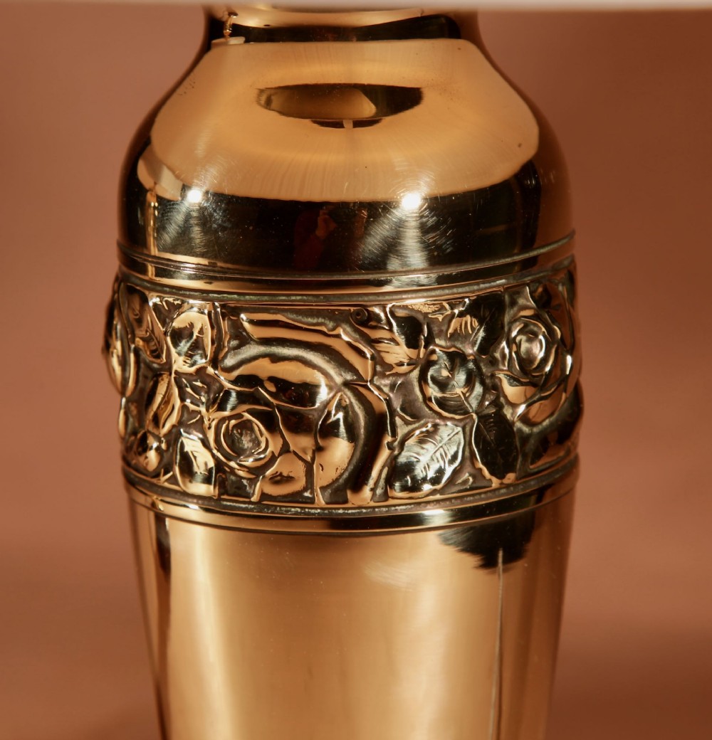 A pair of French Art Deco polished brass urn-form table lamps featuring embossed floral bands on wooden bases with pleated cream shades. View IV