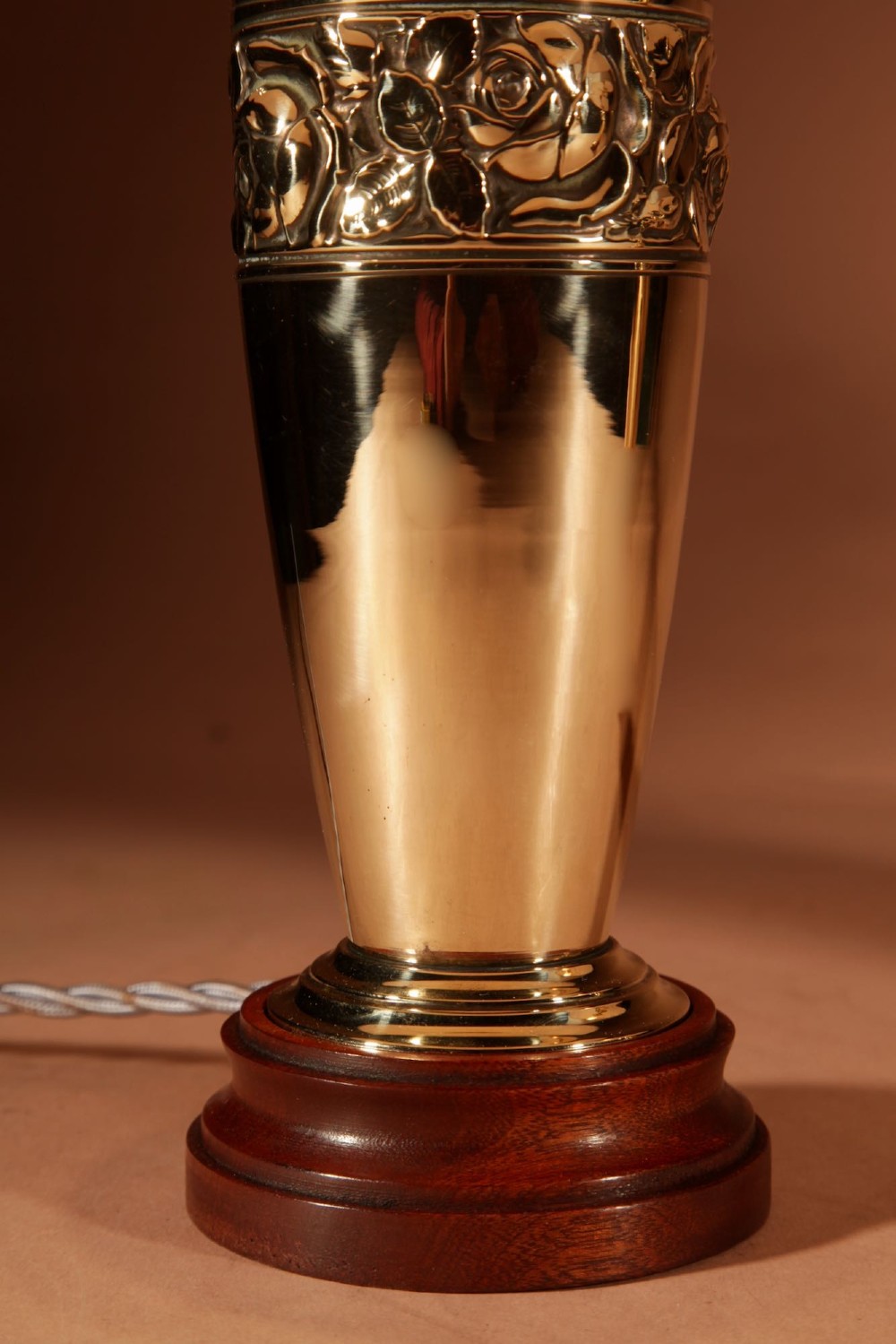 A pair of French Art Deco polished brass urn-form table lamps featuring embossed floral bands on wooden bases with pleated cream shades. View V