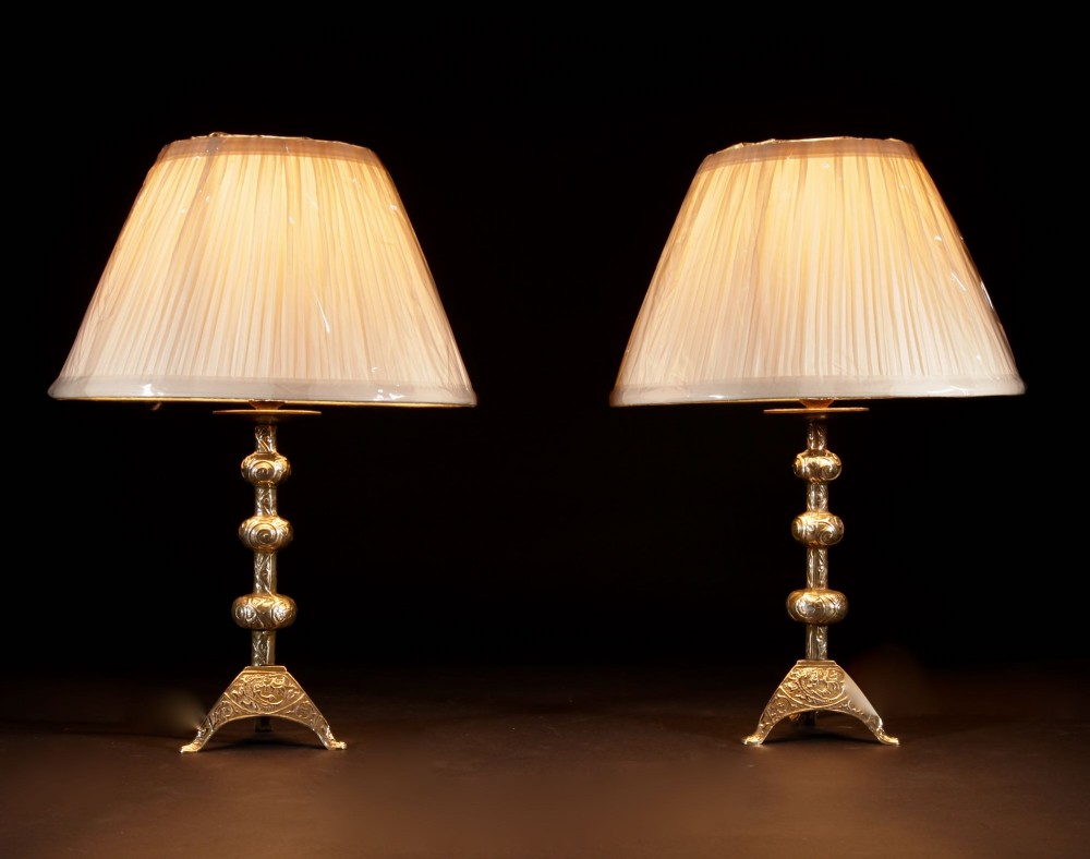 A pair of gold brass table lamps featuring relief-patterned shafts, tripod bases, and cream pleated shades. View III