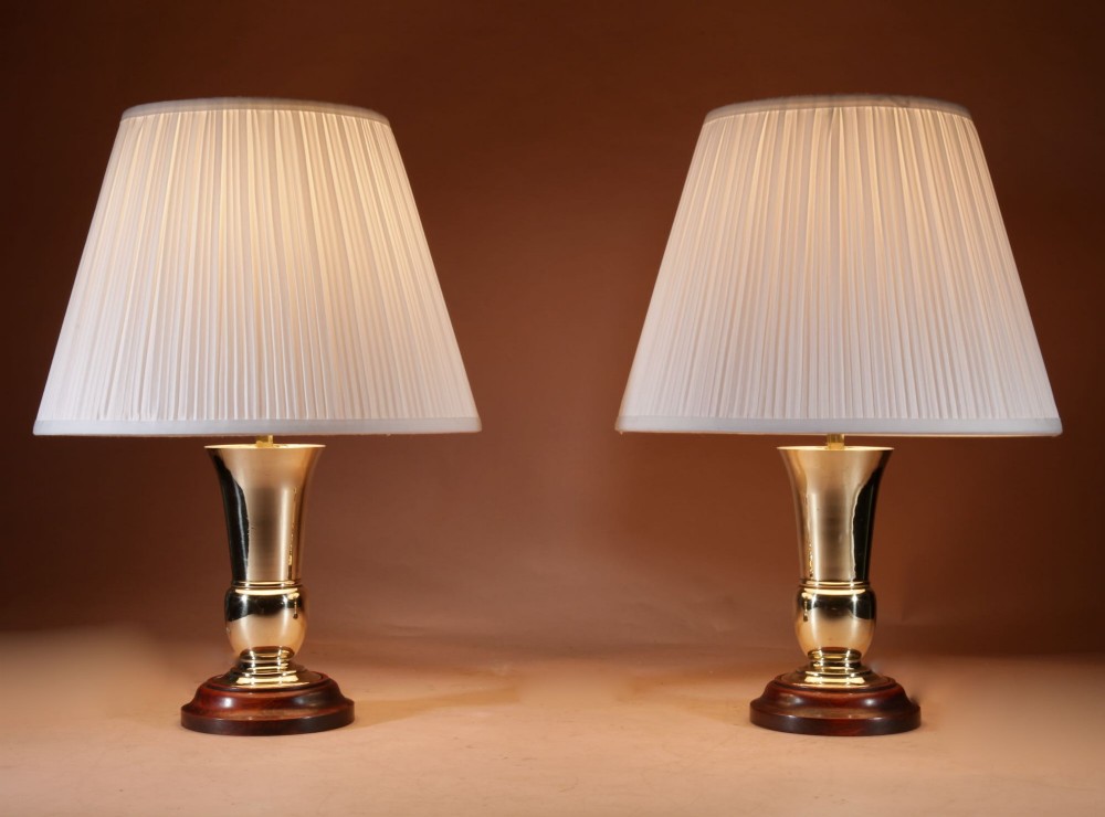 A pair of flared brass vase-form table lamps on circular dark wood bases with off-white pleated shades. View II
