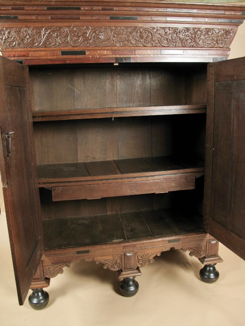 A Dutch Baroque oak armoire featuring two doors with raised geometric cushion panels, rosewood and ebony inlays, a carved frieze, and ebonised ball feet. View II