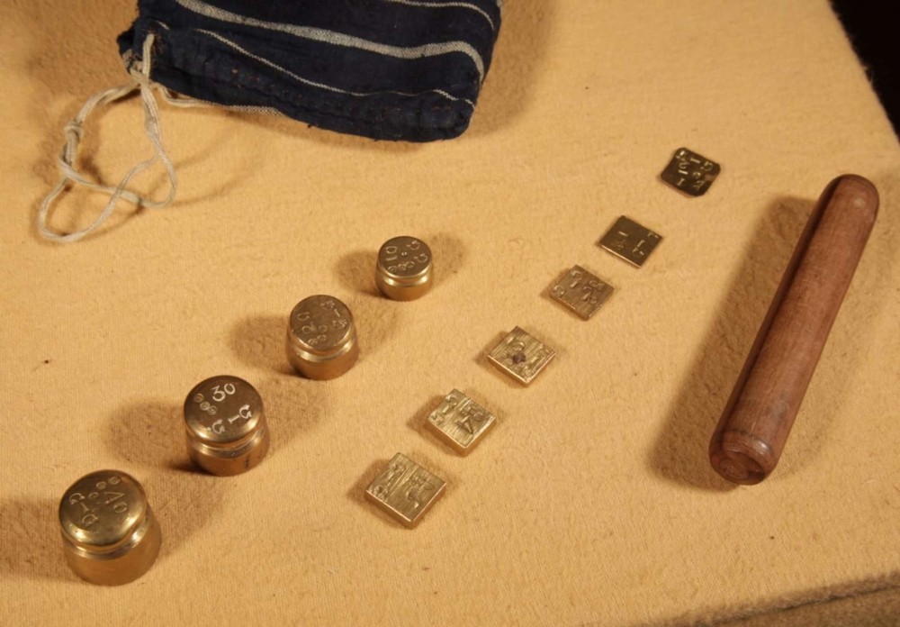 An 1846 Dutch brass bushel balance set featuring a balance beam, two cylindrical brass measuring buckets, calibrated brass weights, a wooden striker, and a striped fabric pouch. View III