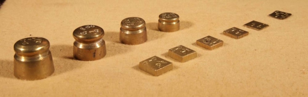 An 1846 Dutch brass bushel balance set featuring a balance beam, two cylindrical brass measuring buckets, calibrated brass weights, a wooden striker, and a striped fabric pouch. View IV