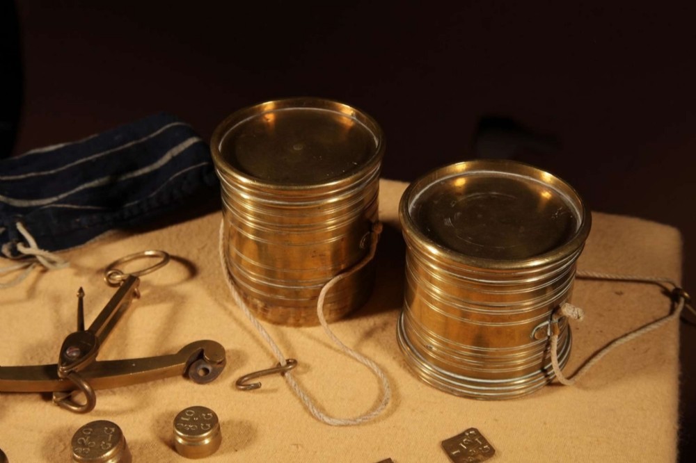 An 1846 Dutch brass bushel balance set featuring a balance beam, two cylindrical brass measuring buckets, calibrated brass weights, a wooden striker, and a striped fabric pouch. View VIII