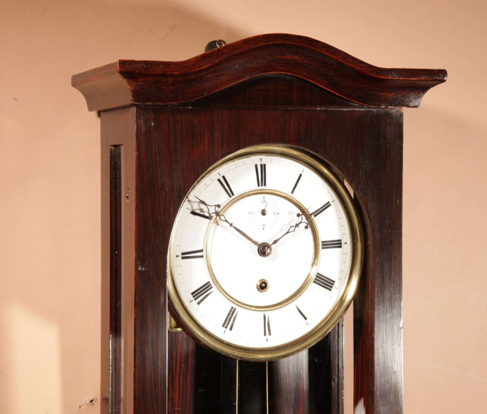An antique dark wood Vienna regulator wall clock featuring a glazed case, white enamel dial with Roman numerals, and a polished brass pendulum. View V
