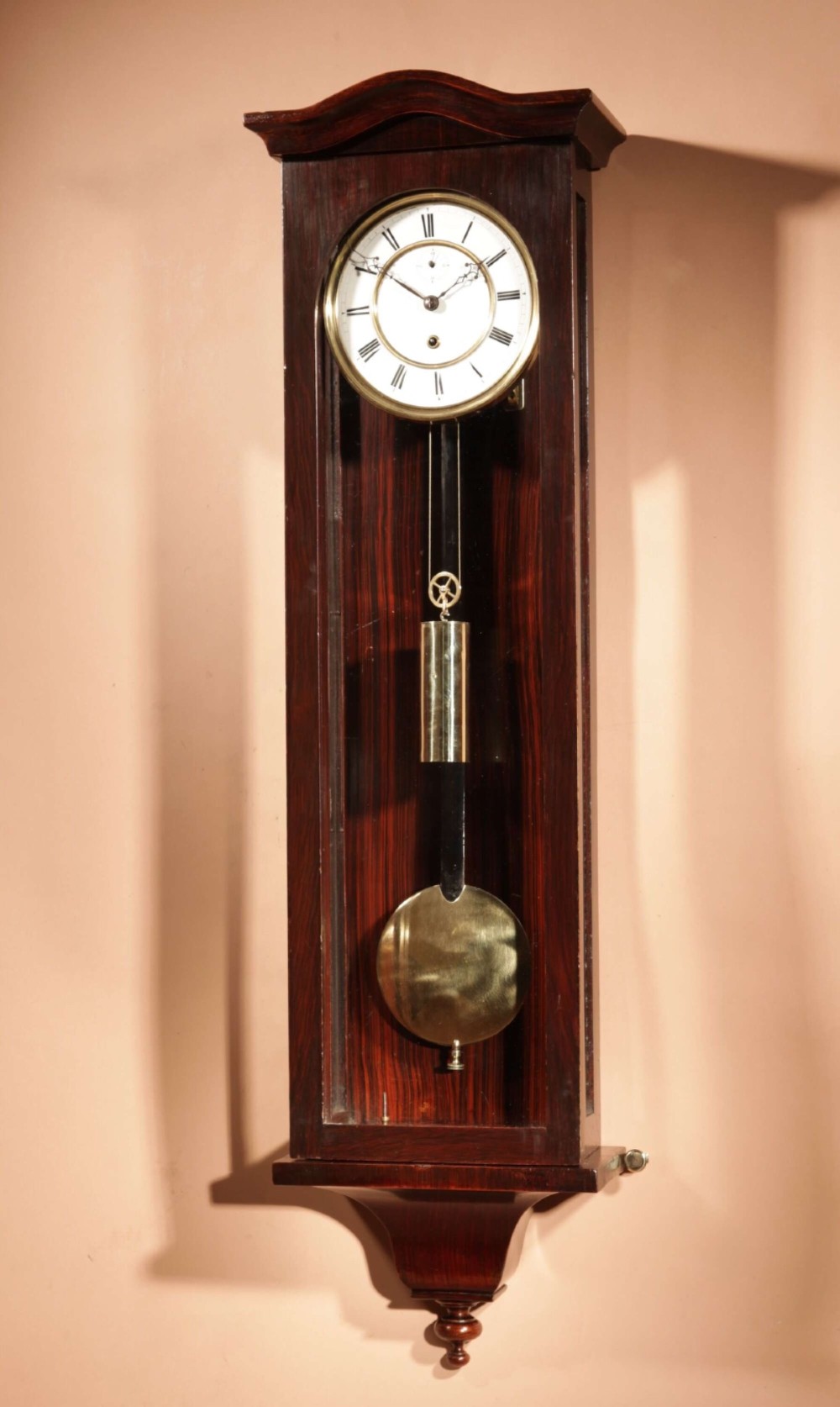 An antique dark wood Vienna regulator wall clock featuring a glazed case, white enamel dial with Roman numerals, and a polished brass pendulum.