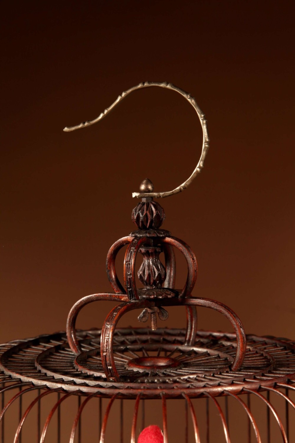 A cylindrical dark carved bamboo Chinese bird cage featuring a metal hanging hook, blue and white porcelain feeding cups, intricate carved plaques, and a matching circular wooden base. View XI
