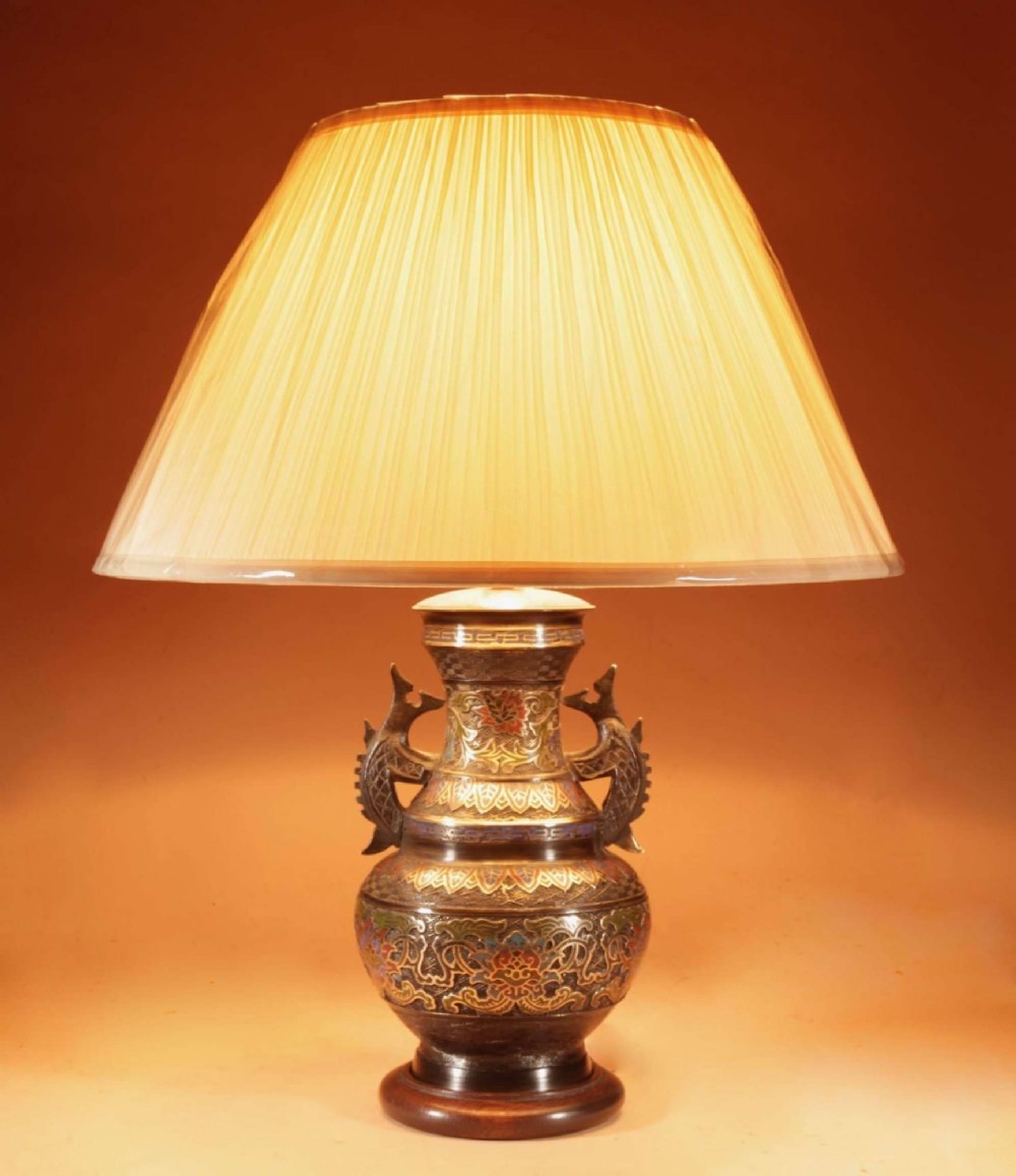 An antique Japanese bronze urn converted into a table lamp, featuring colourful Champleve enamel motifs, twin handles, and a cream pleated shade.