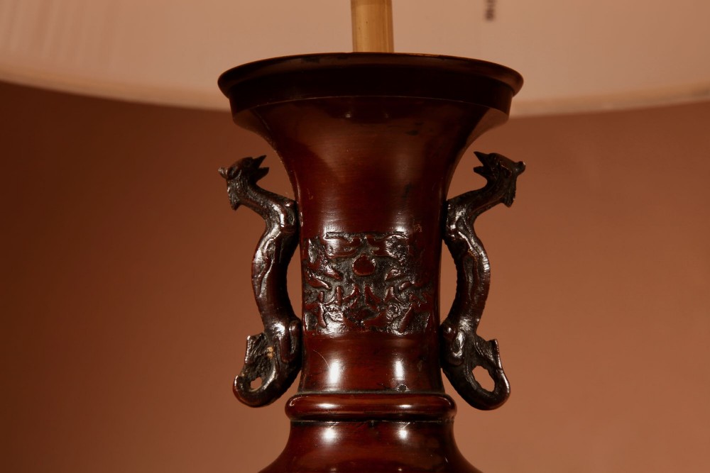 A matching pair of dark patinated bronze vase-shaped table lamps with dragon handles and pleated cream lampshades. View IV