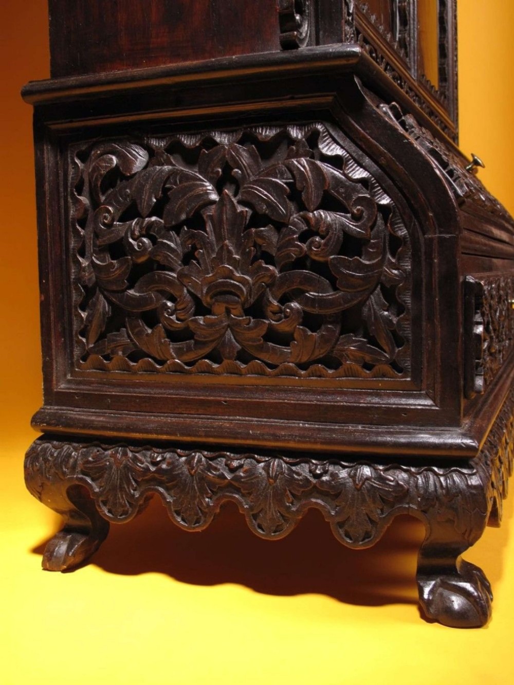 A 19th-century Anglo-Indian dark hardwood small display cabinet featuring intricate pierced foliate carvings, an arched pediment, a glazed four-pane door with scalloped moulding, and two carved drawers at the base. View II