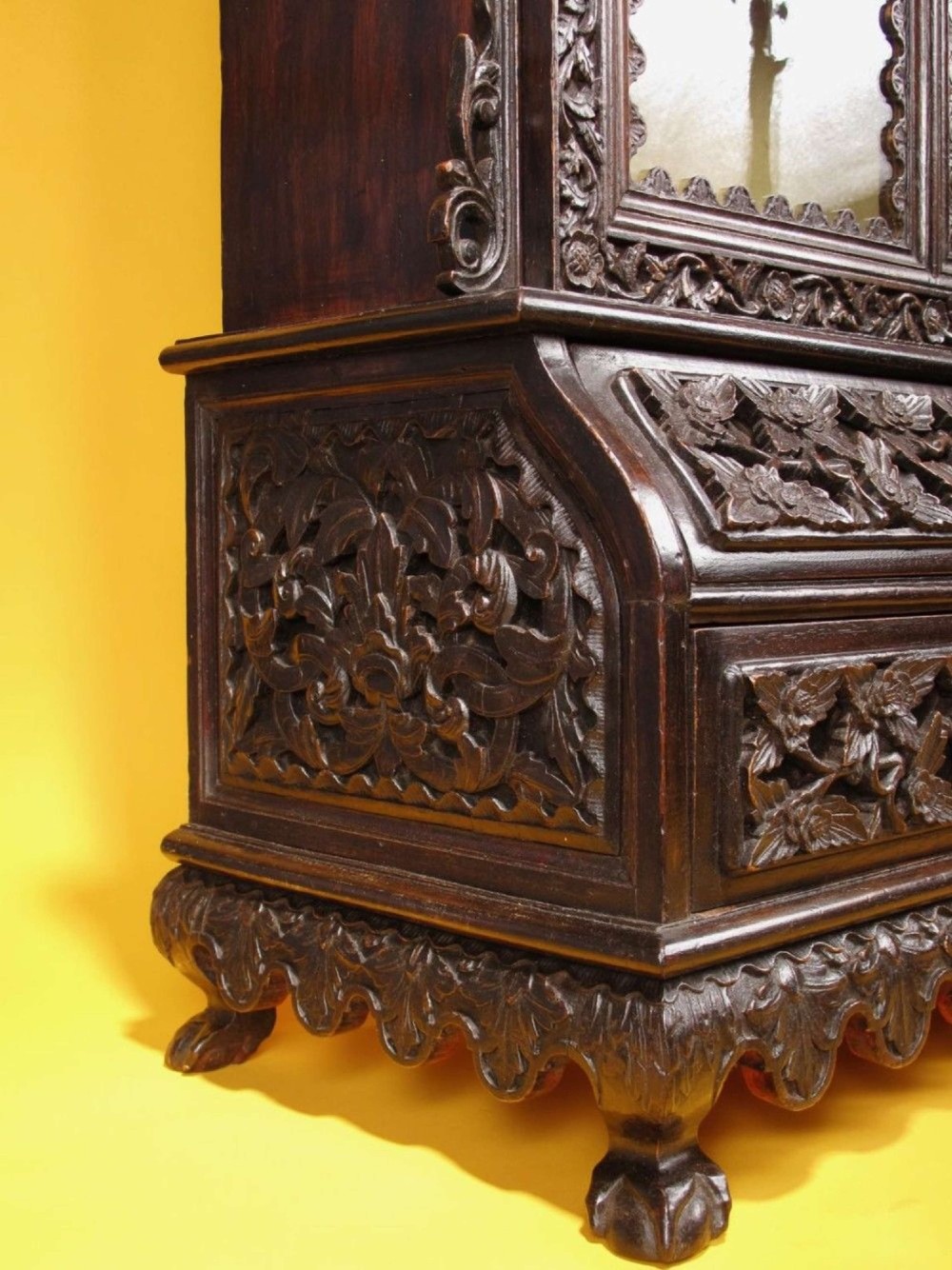 A 19th-century Anglo-Indian dark hardwood small display cabinet featuring intricate pierced foliate carvings, an arched pediment, a glazed four-pane door with scalloped moulding, and two carved drawers at the base. View XIV