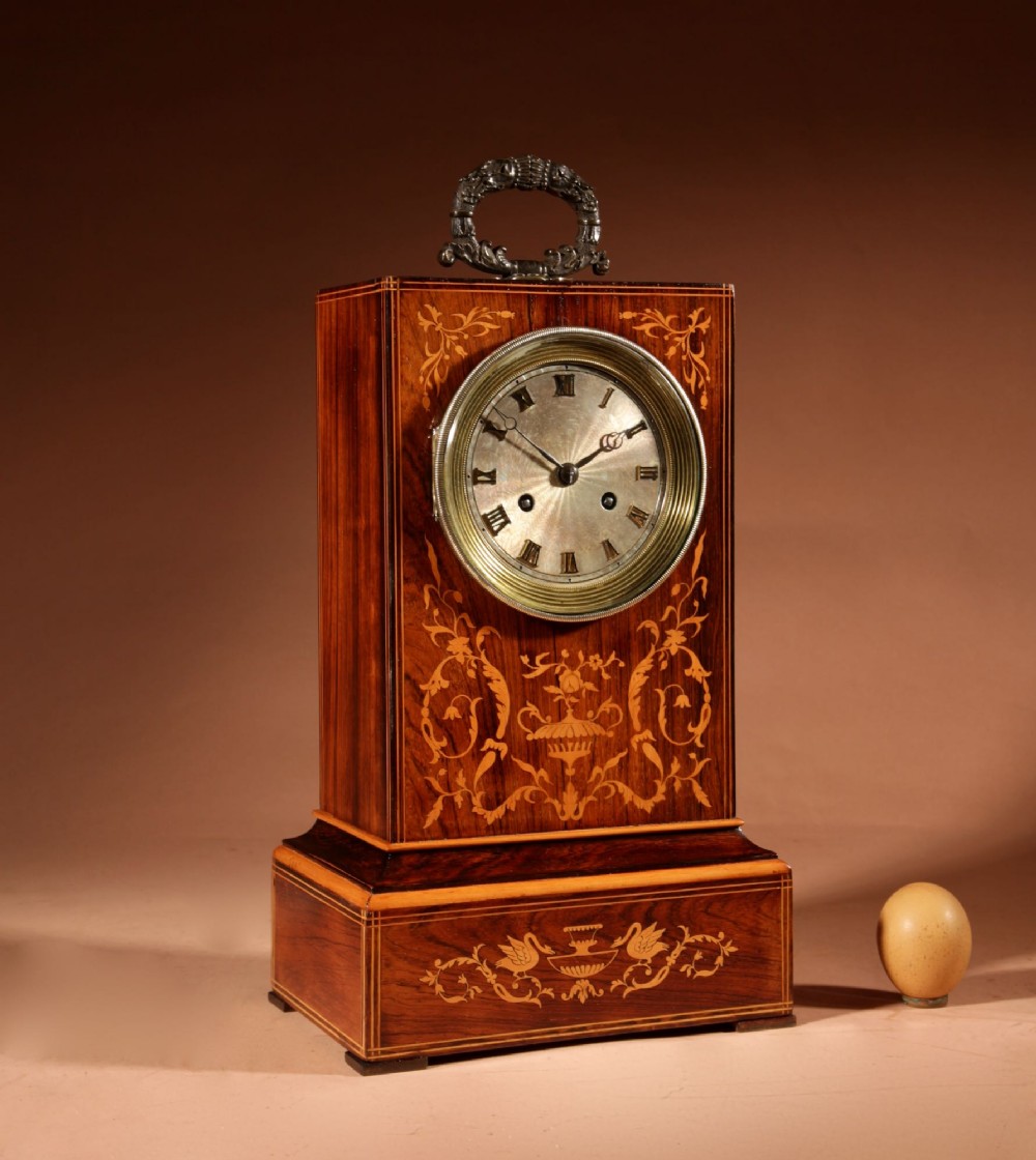An antique Charles X rosewood mantel clock featuring intricate floral marquetry inlays, a silvered Roman numeral dial, and a decorative cast brass handle on top.