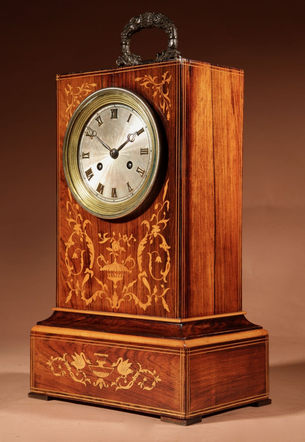 An antique Charles X rosewood mantel clock featuring intricate floral marquetry inlays, a silvered Roman numeral dial, and a decorative cast brass handle on top. View IV